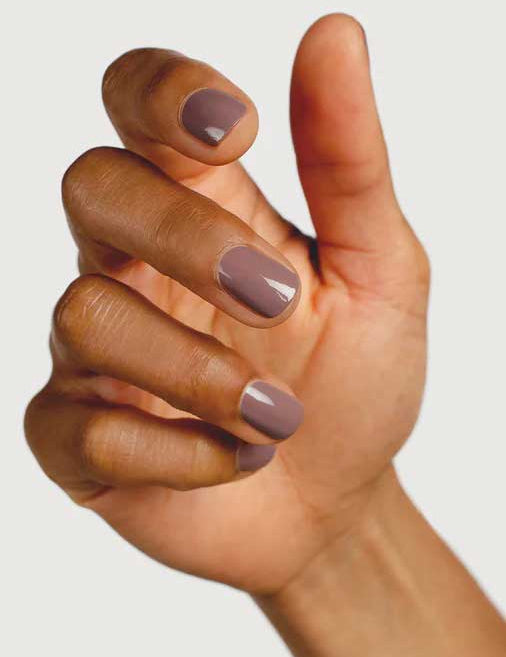 A close-up of a hand with medium brown skin and neatly manicured nails painted in Sienna Byron Bay Nurture, a glossy light mauve shade by Sienna Byron Bay, against a plain light background.