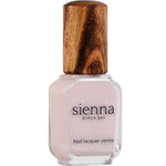A bottle of Sienna Byron Bay Enlightened nail lacquer with pale pink polish, a clear rectangular glass base, and a textured wooden cap. The label reads “Sienna Byron Bay Nail lacquer vernis.”.