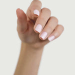 A hand with light skin tone and neatly manicured nails painted in Sienna Byron Bay Enlightened, a pale pink shade by Sienna Byron Bay, is shown with fingers slightly curled against a plain light background.
