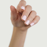 A hand with light skin tone and neatly manicured nails painted in Sienna Byron Bay Enlightened, a pale pink shade by Sienna Byron Bay, is shown with fingers slightly curled against a plain light background.