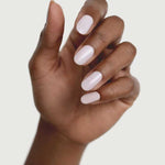 A hand with medium brown skin is shown against a light background, displaying neatly manicured nails painted in Sienna Byron Bay Enlightened, a glossy pale pink or white shade by Sienna Byron Bay.