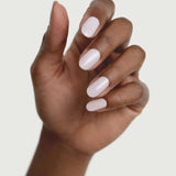 A hand with medium brown skin is shown against a light background, displaying neatly manicured nails painted in Sienna Byron Bay Enlightened, a glossy pale pink or white shade by Sienna Byron Bay.