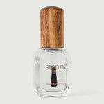 A clear glass bottle of Sienna Byron Bay Glossy Top Coat with a wooden cap, containing transparent polish, stands upright on a light gray background.