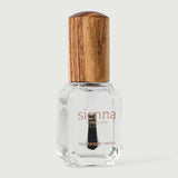 A clear glass bottle of Sienna Byron Bay Glossy Top Coat with a wooden cap, containing transparent polish, stands upright on a light gray background.