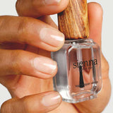 A hand holds a clear bottle of Sienna Byron Bay Glossy Top Coat with a wooden cap, displaying natural, clean nails.