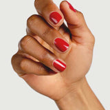 A hand with medium brown skin displays neatly manicured nails painted in Sienna Byron Bay’s Heart, a glossy red shade, against a plain white background.