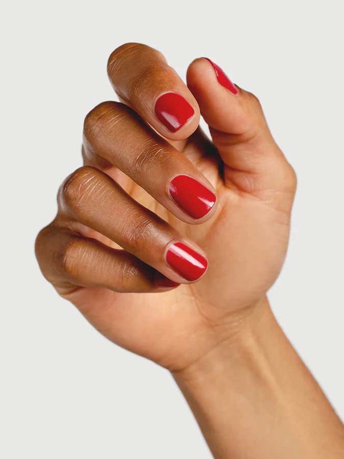 A hand with medium brown skin displays neatly manicured nails painted in Sienna Byron Bay’s Heart, a glossy red shade, against a plain white background.