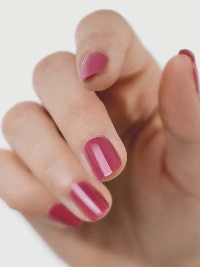 A close-up of a hand with short nails painted in Sienna Byron Bay Heartspace pink polish by Sienna Byron Bay, set against a plain, light background.