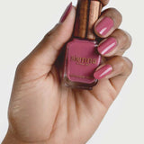 A hand with pink painted nails holds a bottle of Sienna Byron Bay Heartspace nail polish with a wooden cap, matching the nail color, against a plain white background.