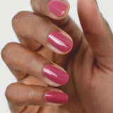 A close-up of a hand with medium brown skin, featuring neatly manicured nails painted with Sienna Byron Bay Heartspace by Sienna Byron Bay, a glossy pink nail polish, against a light background.