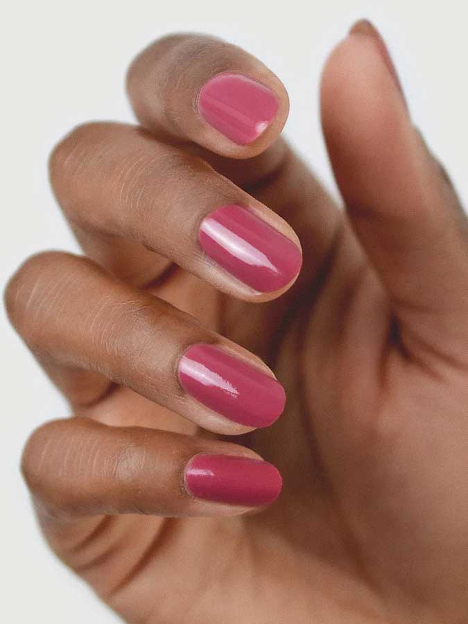 A close-up of a hand with medium brown skin, featuring neatly manicured nails painted with Sienna Byron Bay Heartspace by Sienna Byron Bay, a glossy pink nail polish, against a light background.