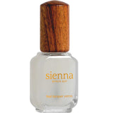 A clear glass bottle of Sienna Byron Bay Matte Top Coat with a wooden cap. The yellow label reads sienna BYRON BAY and Matte Top Coat. The bottle holds a white or pale matte top coat nail polish.