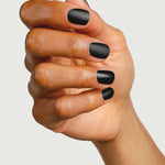 A hand with short, neatly manicured nails painted in matte black, finished with Sienna Byron Bay Matte Top Coat by Sienna Byron Bay, is shown against a plain light background.