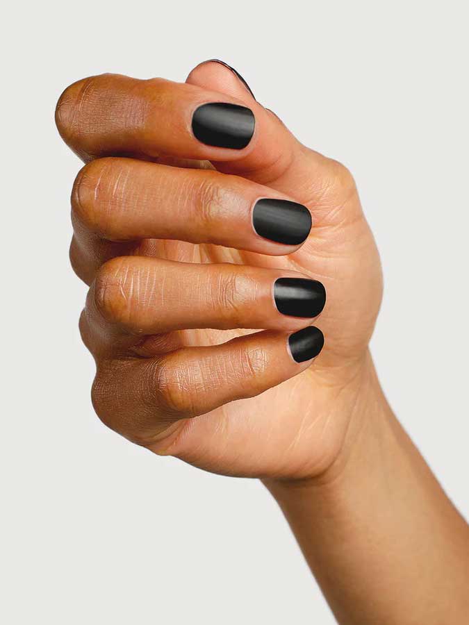 A hand with short, neatly manicured nails painted in matte black, finished with Sienna Byron Bay Matte Top Coat by Sienna Byron Bay, is shown against a plain light background.