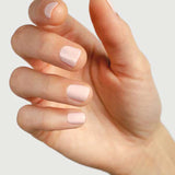 A close-up of a light-skinned hand with neatly manicured nails painted in Sienna Byron Bay Melody, a pale pink shade by Sienna Byron Bay, set against a plain light background.