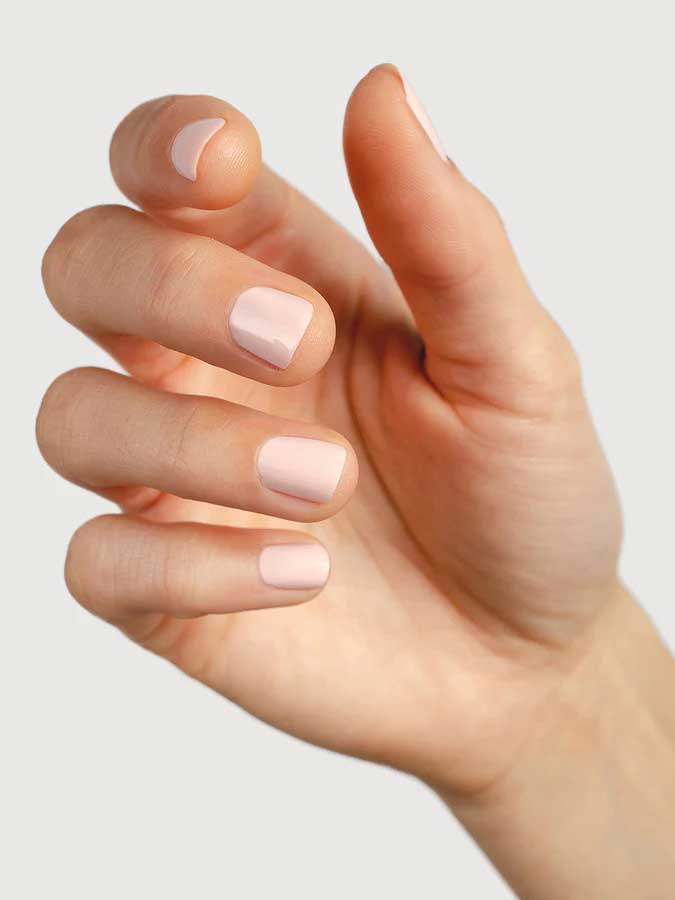 A close-up of a light-skinned hand with neatly manicured nails painted in Sienna Byron Bay Melody, a pale pink shade by Sienna Byron Bay, set against a plain light background.