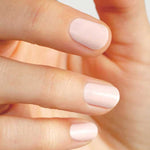 A close-up of a hand with neatly manicured, short nails painted in Sienna Byron Bay Melody, a pale pink shade by Sienna Byron Bay. The fingers are slightly bent and the nails are evenly shaped.