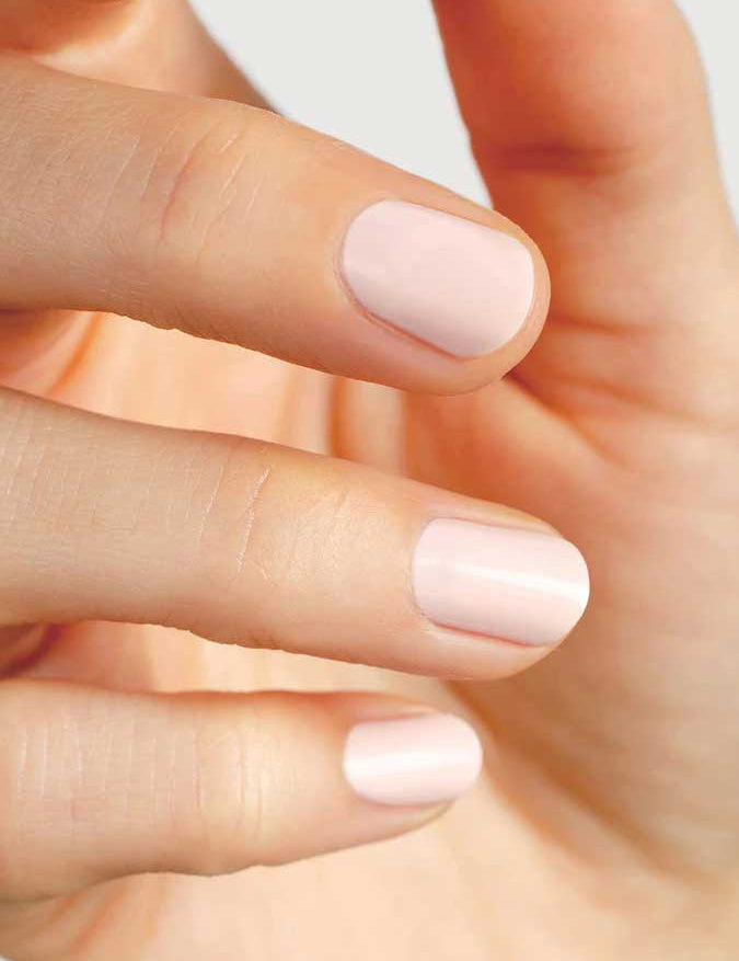 A close-up of a hand with neatly manicured, short nails painted in Sienna Byron Bay Melody, a pale pink shade by Sienna Byron Bay. The fingers are slightly bent and the nails are evenly shaped.