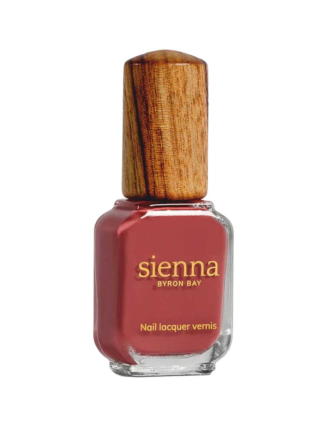 A bottle of Sienna Byron Bay Muse nail lacquer, a reddish-pink shade, features a unique wooden cap and gold text on the glass.