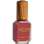 A bottle of Sienna Byron Bay Muse nail lacquer, a reddish-pink shade, features a unique wooden cap and gold text on the glass.