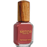A bottle of Sienna Byron Bay Muse nail lacquer, a reddish-pink shade, features a unique wooden cap and gold text on the glass.