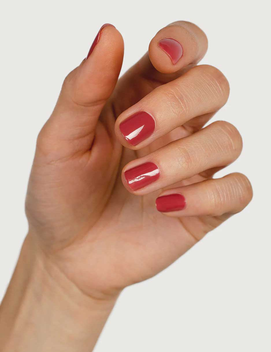 A close-up of a hand with neatly manicured nails painted in Sienna Byron Bay Muse, a glossy red polish by Sienna Byron Bay, set against a plain white background.