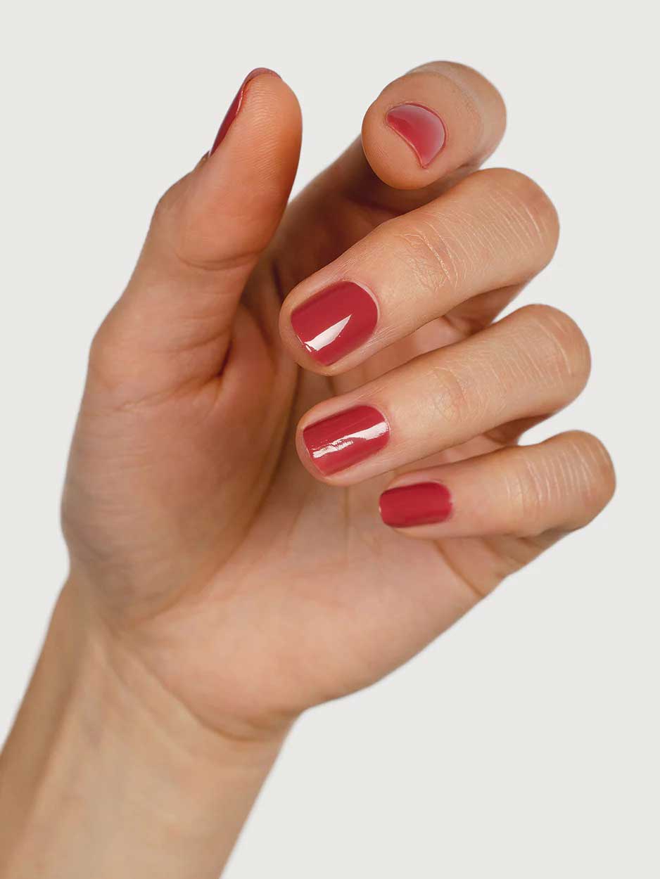 A close-up of a hand with neatly manicured nails painted in Sienna Byron Bay Muse, a glossy red polish by Sienna Byron Bay, set against a plain white background.