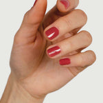 A close-up of a hand with neatly manicured nails painted in Sienna Byron Bay Muse, a glossy red polish by Sienna Byron Bay, set against a plain white background.
