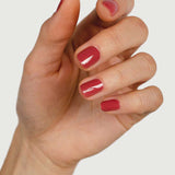 A close-up of a hand with neatly manicured nails painted in Sienna Byron Bay Muse, a glossy red polish by Sienna Byron Bay, set against a plain white background.