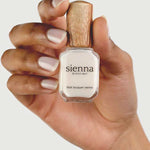 A hand with neatly manicured nails holds a bottle of Sienna Byron Bay - Hope nail lacquer with a wooden cap against a light background.