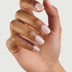 A hand with medium brown skin tone is shown against a plain background, fingers slightly curled. The neatly manicured nails are painted with Sienna Byron Bay - Hope by Sienna Byron Bay, a pale, natural-looking polish.