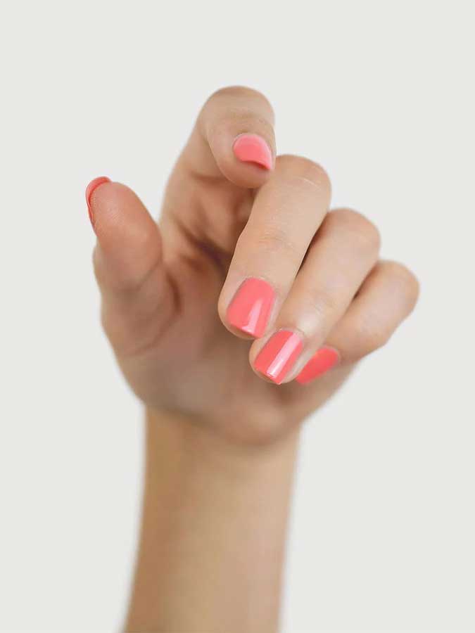 A hand with fingers slightly bent displays fingernails painted in Sienna Byron Bay Laughter, a glossy pink shade by Sienna Byron Bay, against a plain white background.