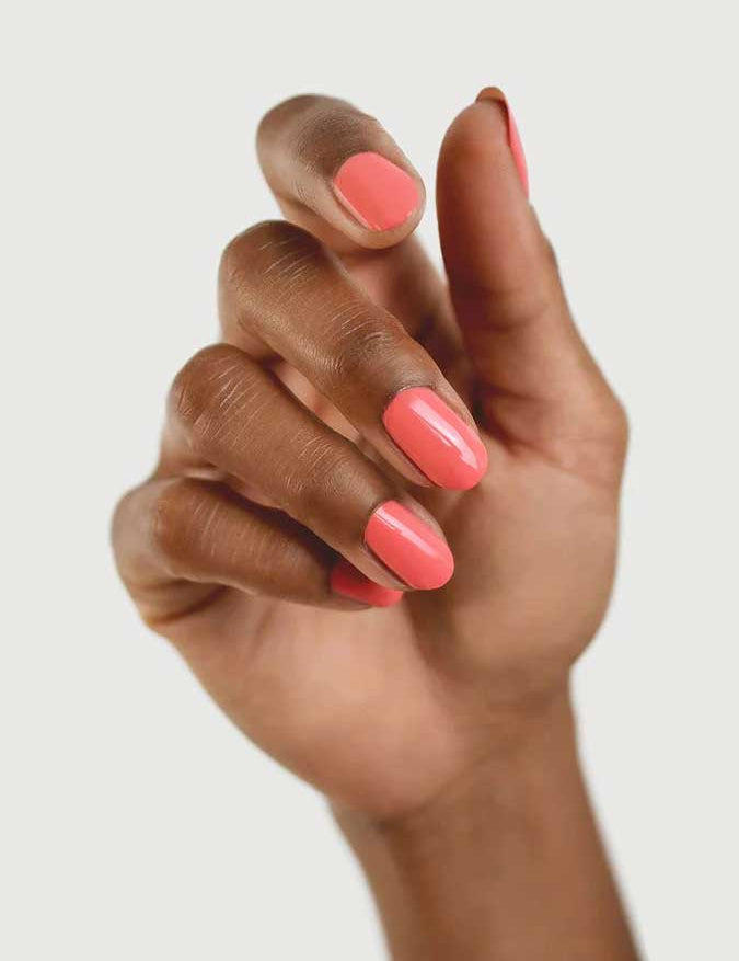 A hand with medium brown skin displays neatly manicured nails painted in Sienna Byron Bay Laughter, a glossy pink shade by Sienna Byron Bay, against a plain light background.