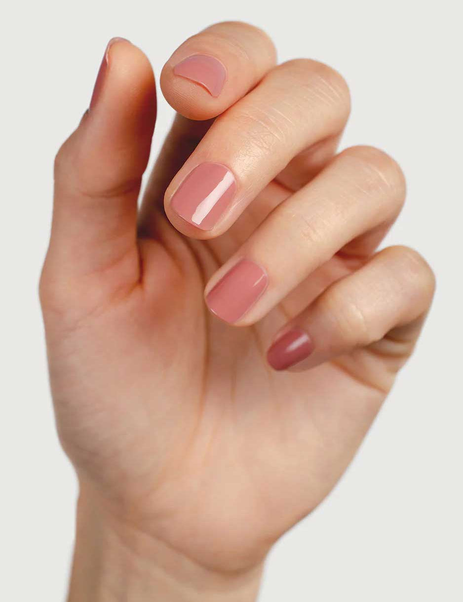 A close-up of a hand with neatly manicured nails painted in Sienna Byron Bay Nail Polish - Stone, a glossy nude-pink shade by Sienna Byron Bay, set against a plain, light background.