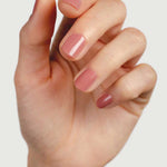A close-up of a hand with neatly manicured nails painted in Sienna Byron Bay Nail Polish - Stone, a glossy nude-pink shade by Sienna Byron Bay, set against a plain, light background.