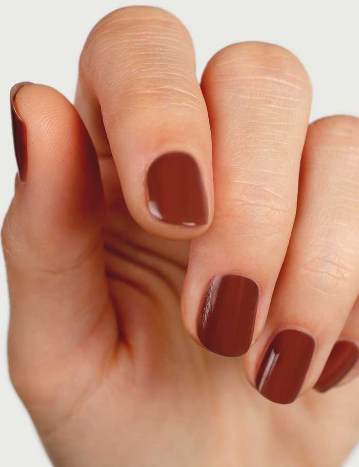 A close-up of a hand with short, neatly manicured nails painted in Sienna Byron Bay Nail Polish - Sienna, a plant-derived, toxin-free glossy burnt umber shade.
