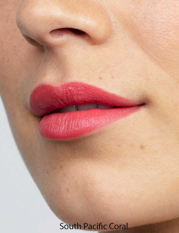 Close-up of smooth lips wearing Antipodes Moisture Boost Natural Lipsticks 4g in coral pink, with an even, moisturizing finish. Text below reads South Pacific Coral.