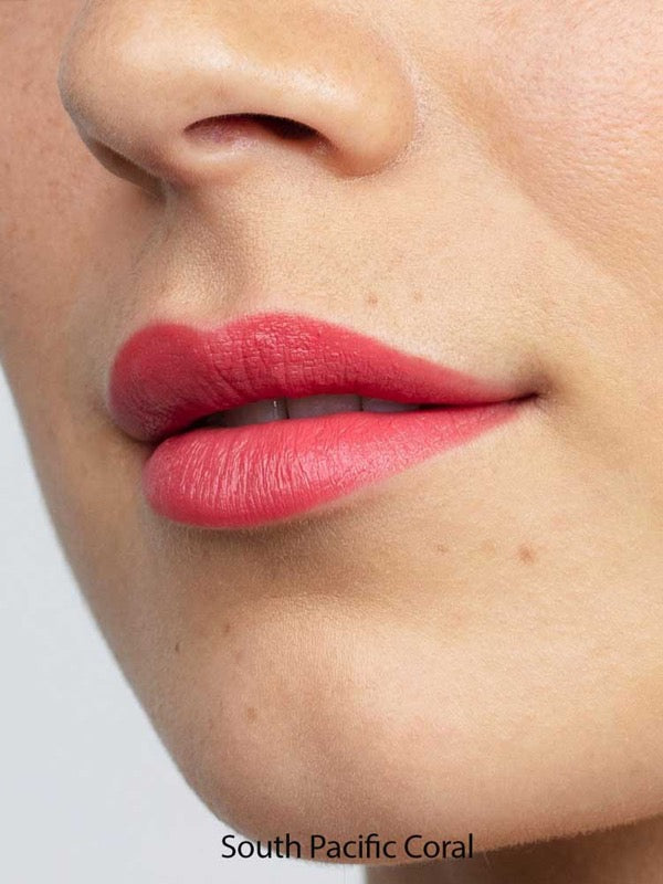 Close-up of smooth lips wearing Antipodes Moisture Boost Natural Lipsticks 4g in coral pink, with an even, moisturizing finish. Text below reads South Pacific Coral.