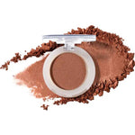 An open round compact of 100% Pure Fruit Pigmented® Eye Shadow 2g by 100% Pure displays its pressed powder, with loose vegan eyeshadow scattered around it on a clean white background.
