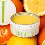 An open tin of Tuttofare Sicilian Citrus Tallow Balm 70g, made with grass-fed beef tallow, sits among sliced lemons, limes, and oranges. Its hydrating yellow balm and dewy tin capture the essence of pure citrus freshness.