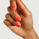 A hand with medium skin tone displays neatly manicured nails painted in Sienna Byron Bay Nail Polish - Tango, a glossy tangerine orange shade, against a plain background.