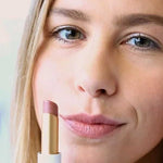 A woman with light skin applies Luk Beautifood Lip Nourish Lipsticks 3g in Tea Rose, holding the mauve-pink tube near her face. The words "Tea Rose" appear at the bottom of the image.