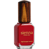 A bottle of Sienna Byron Bay Nail Polish - Tempest, featuring a square glass base, gold lettering, plant-derived red formula, and a dark wooden cap against a white background.