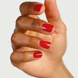 A hand with medium brown skin displays glossy, plant-derived Sienna Byron Bay Nail Polish in the shade Tempest, fingers gently curved against a light neutral background.