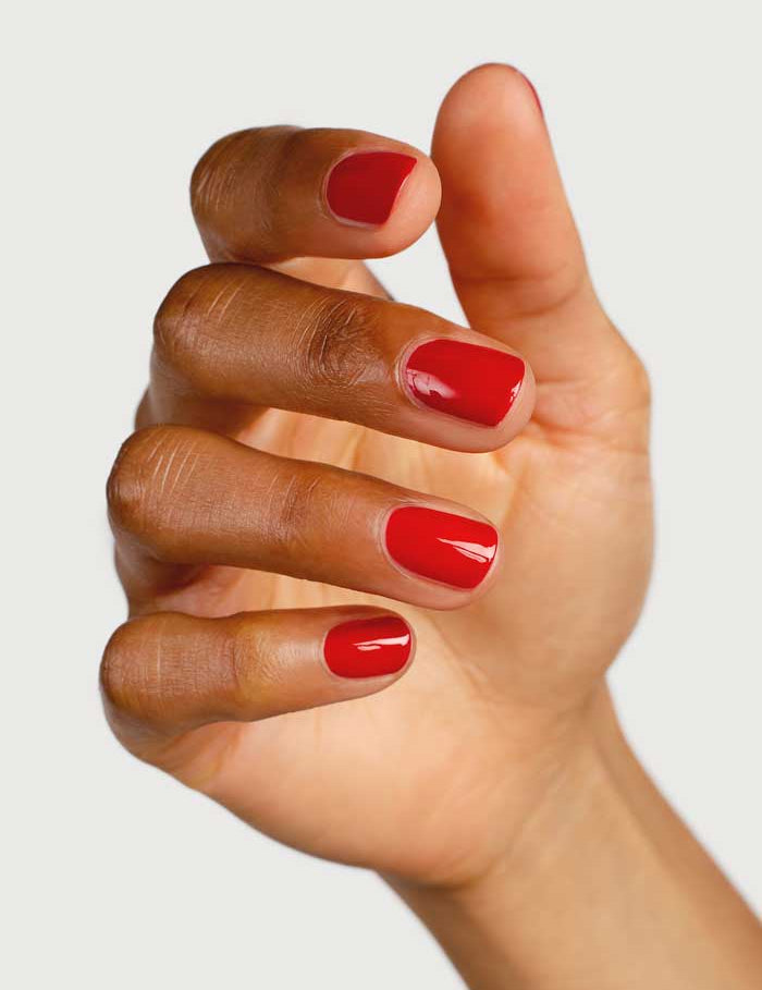 A hand with medium brown skin displays glossy, plant-derived Sienna Byron Bay Nail Polish in the shade Tempest, fingers gently curved against a light neutral background.
