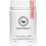 A white container of The Beauty Chef GUT PRIMER+® 140g with a pink tag on the lid. The label highlights “Soothe, Debloat, Restore” and describes it as an advanced gut health powder with GutGard for abdominal bloating relief.