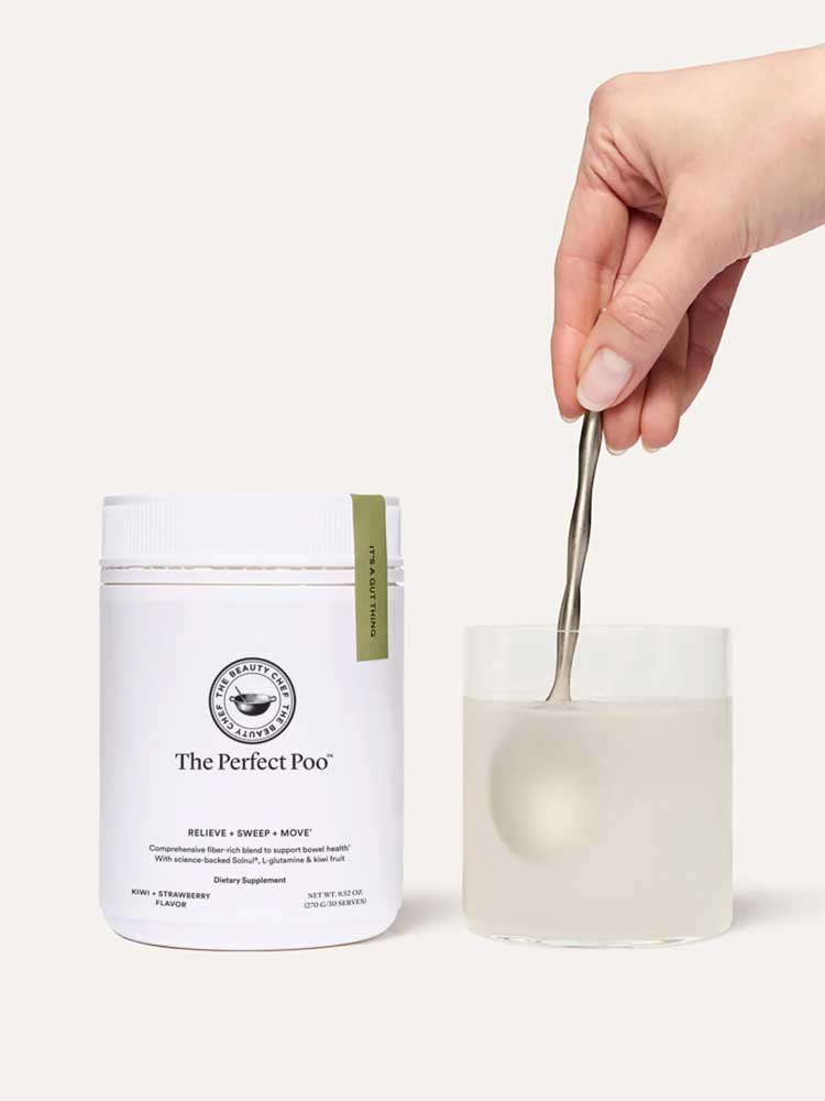 A hand stirs a drink with a spoon in a clear glass beside a white container labeled The Beauty Chef The Perfect Poo™ 270g, a fibre supplement with resistant starch that supports digestive health.