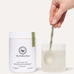 A hand stirs a drink with a spoon in a clear glass beside a white container labeled The Beauty Chef The Perfect Poo™ 270g, a fibre supplement with resistant starch that supports digestive health.