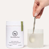 A hand stirs a drink with a spoon in a clear glass beside a white container labeled The Beauty Chef The Perfect Poo™ 270g, a fibre supplement with resistant starch that supports digestive health.