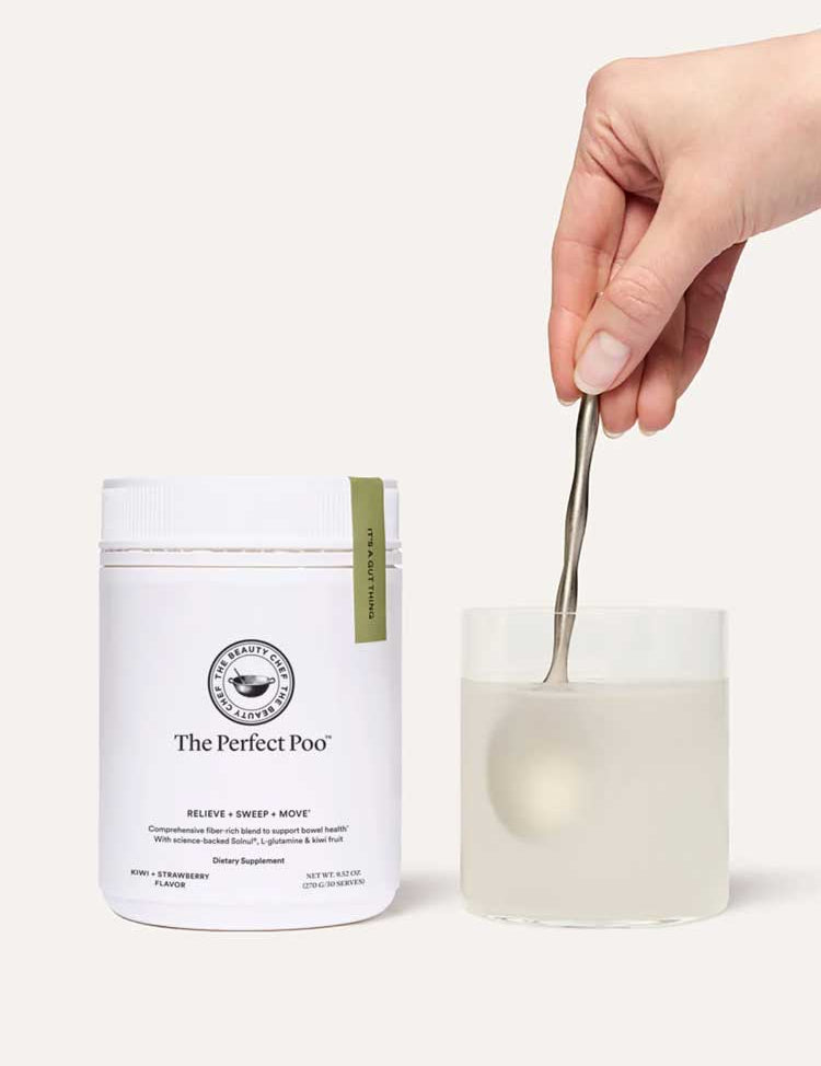 A hand stirs a drink with a spoon in a clear glass beside a white container labeled The Beauty Chef The Perfect Poo™ 270g, a fibre supplement with resistant starch that supports digestive health.